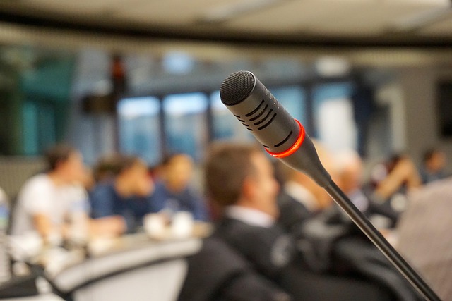 L’immagine mostra un microfono in primo piano, pronto per un intervento pubblico, mentre sullo sfondo si intravede una sala con persone sedute che partecipano a un incontro o a una conferenza. La scena richiama un contesto di dialogo e partecipazione collettiva. Nel progetto “Internazionale per la Pace”, questa immagine rappresenta gli spazi di ascolto e confronto in cui studiosi, rappresentanti culturali e cittadini possono condividere riflessioni e prospettive sulla storia, sulla pace e sulle relazioni tra i popoli.