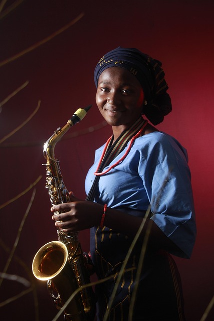L’immagine mostra una giovane donna sorridente che tiene in mano un saxofono durante una performance musicale. Lo sfondo è illuminato da una luce calda che mette in risalto il volto della musicista. L’immagine richiama la vitalità culturale della società cubana e la capacità della cultura e della musica di esprimere identità e resilienza.