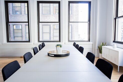 L’immagine mostra una sala riunioni luminosa con un lungo tavolo circondato da sedie. Grandi finestre lasciano entrare la luce naturale e permettono di vedere gli edifici all’esterno. L’ambiente richiama uno spazio di confronto e discussione. Nel contesto dell’articolo, l’immagine suggerisce l’idea di dialogo tra prospettive diverse e la riflessione sulla pluralità delle esperienze storiche e culturali.