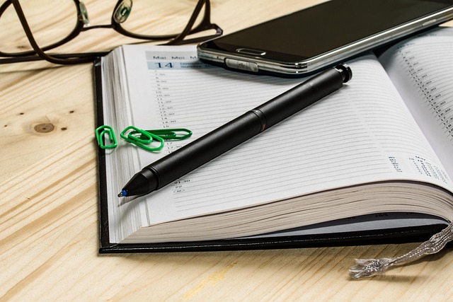 L’immagine mostra un’agenda aperta su una scrivania, accanto a una penna, uno smartphone e un paio di occhiali. Gli oggetti suggeriscono un momento di pianificazione e organizzazione delle attività. Nel contesto del progetto “Internazionale per la Pace”, l’immagine rappresenta il lavoro di programmazione e sviluppo degli incontri pubblici che accompagnano il percorso espositivo e favoriscono il dialogo tra realtà culturali e istituzionali.